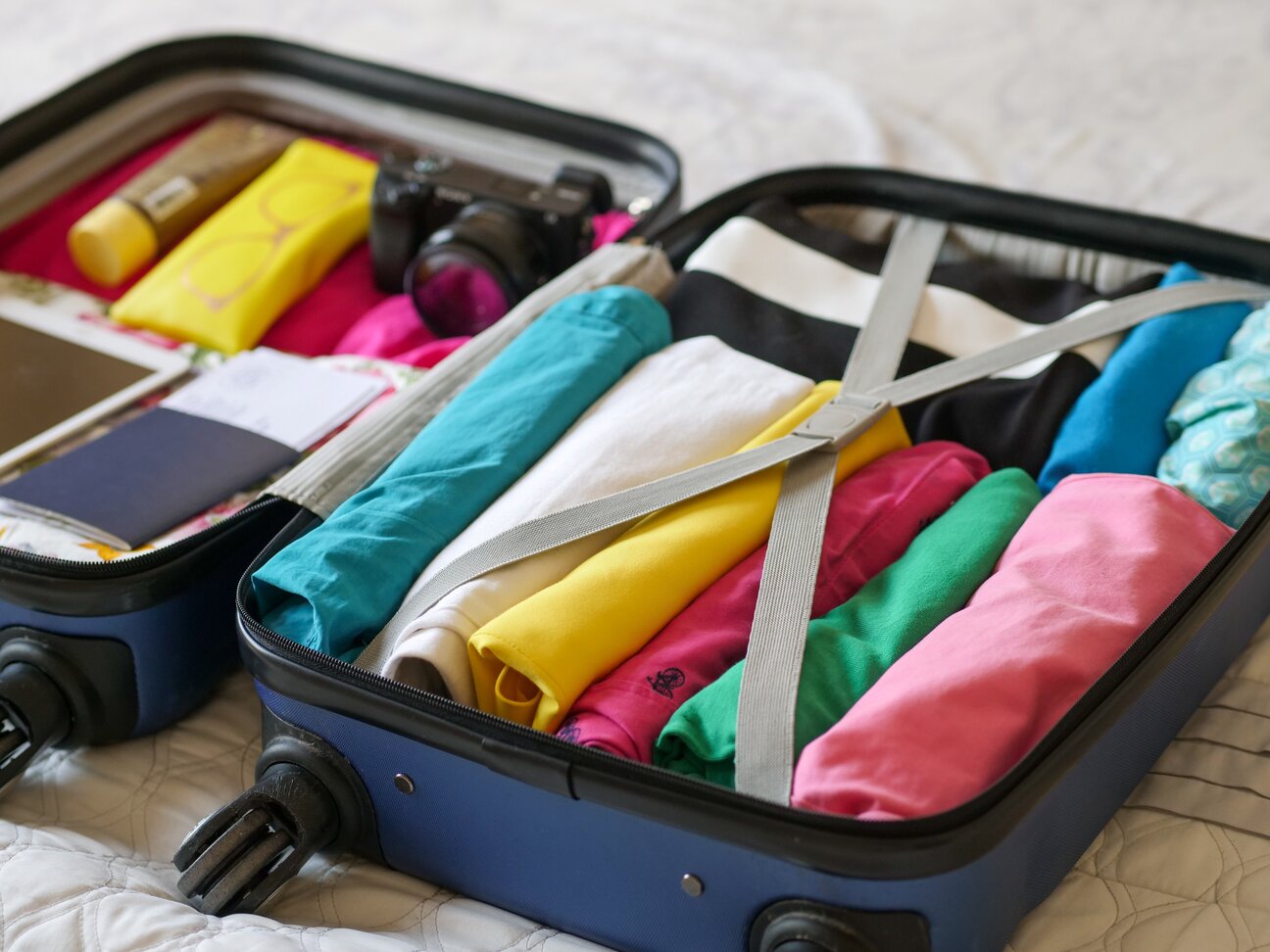 открытый чемодан с вещами: одежда, фотоаппарат, документы, футляр для очков, крем