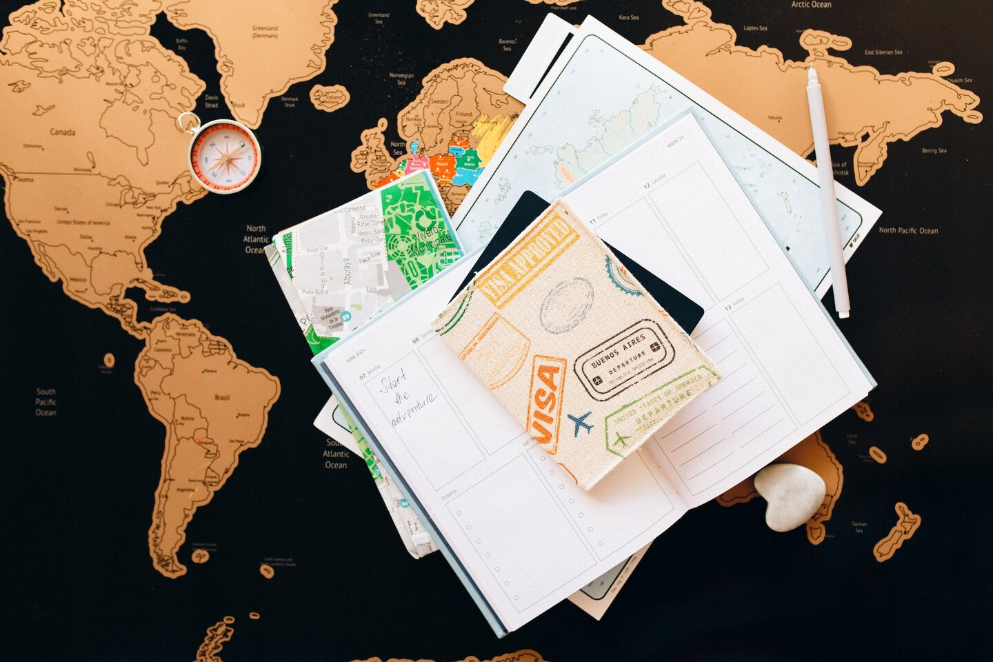 документы, компас, ручка и безделушка в форме сердца лежат на карте мира